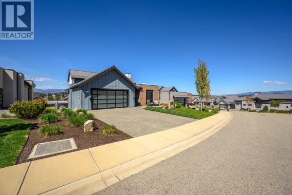 Street view showing the modern home's driveway, landscaping, and surrounding houses. - 291 Grange Drive, Vernon