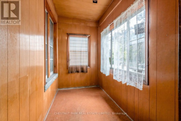 Interior enclosed porch with wood paneled walls, windows with lace curtains, and an orange floor. - 291 St Helen's Avenue, Toronto