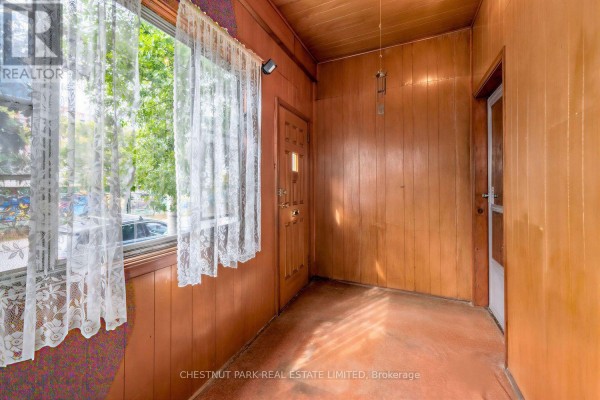 Interior enclosed porch with wood paneled walls, a front door, windows with lace curtains, and an orange floor. - 291 St Helen's Avenue, Toronto
