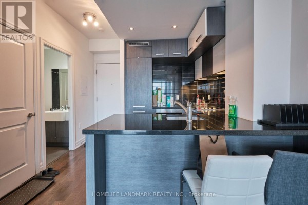 View of a modern kitchen with dark wood cabinets, granite island, and view into a bathroom. - 2910 - 8 The Esplanade, Toronto