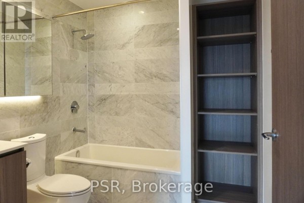 Bathroom with marble tile walls, a bathtub, toilet, and a tall wooden shelving unit. - 2911 - 19 Bathurst Street, Toronto