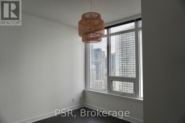 Empty room with large windows offering a city view of Toronto skyscrapers, and a decorative woven pendant light. - 2911 - 19 Bathurst Street, Toronto
