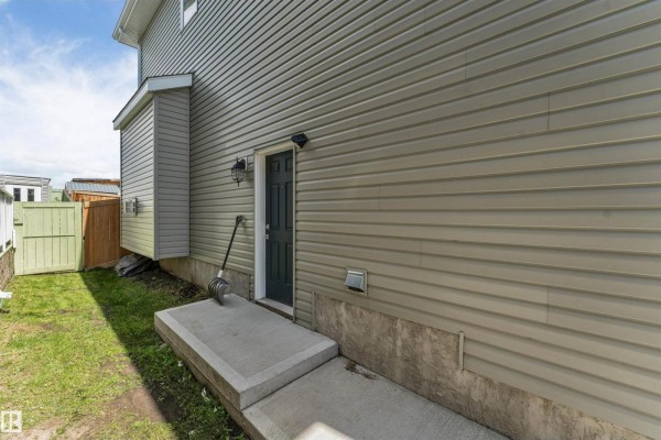 Back exterior view of a house showing beige vinyl siding, a dark door, and a concrete walkway. - 2912 12 Av Nw, Edmonton