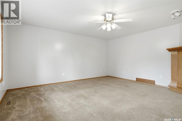 Living room with beige carpet, white walls, and a light wood trim fireplace surround. - 292 Regina Avenue, Katepwa Beach