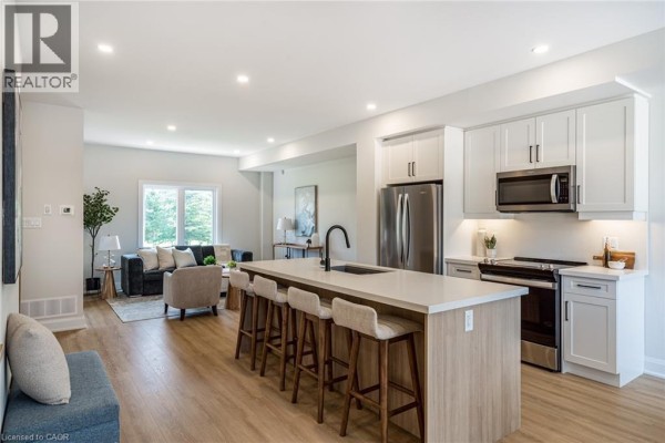 Kitchen with island seating, stainless steel appliances, and adjacent living room. - 292 Vine Street Unit# 82, St  Catharines