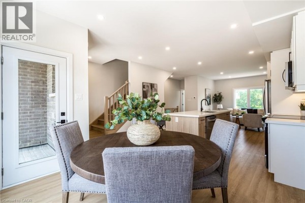 Round dining table with chairs, next to a kitchen island and door. - 292 Vine Street Unit# 82, St  Catharines