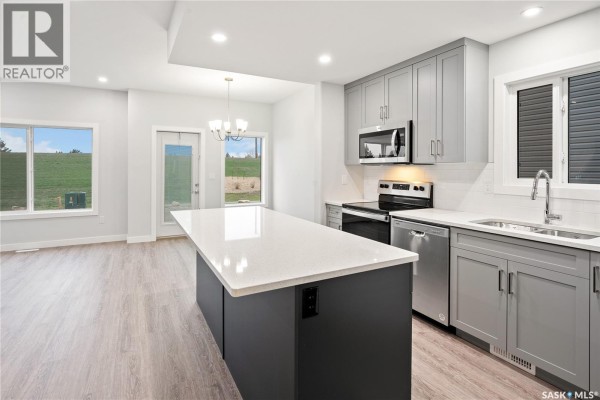 Modern kitchen with gray cabinets, white quartz island, and stainless steel appliances. - 2921 Green Turtle Road, Regina