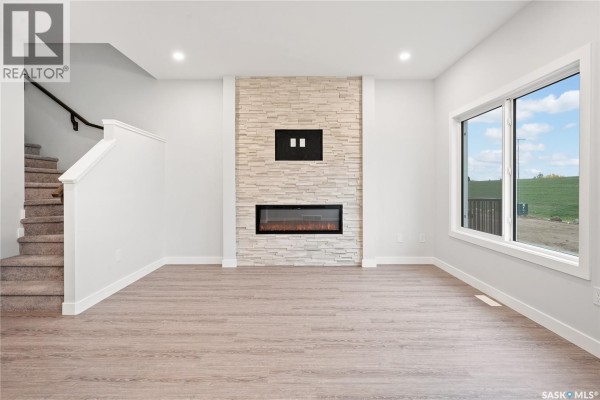 Living room with a stone fireplace and a large window showing a green hill. - 2921 Green Turtle Road, Regina