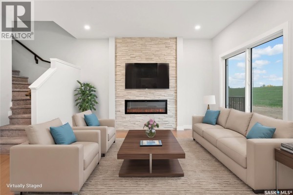 Staged living room with sofas, armchairs, a coffee table, and a stone fireplace. - 2921 Green Turtle Road, Regina