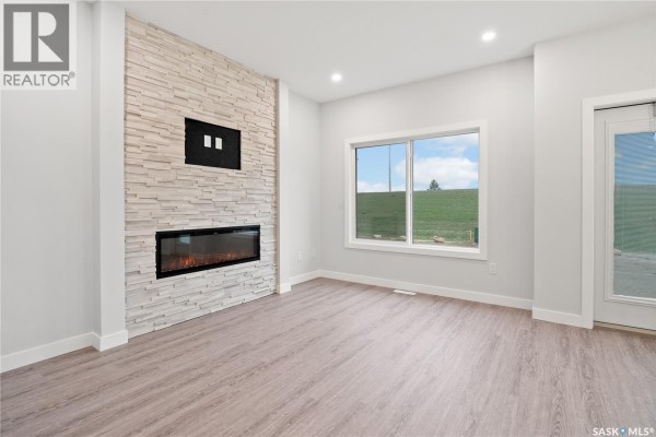 Living room featuring a modern fireplace, stone accent wall, and a large window. - 2921 Green Turtle Road, Regina