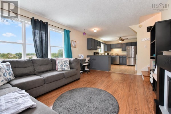 Living room with a large grey sectional sofa, wood laminate flooring, and an open view of the kitchen area. - 2925 No. 7 Hwy, Lake Echo