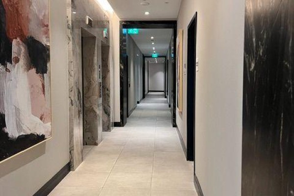 Interior hallway with light grey floor tiles, elevator doors, and abstract art. - 293 The Kingsway, Toronto