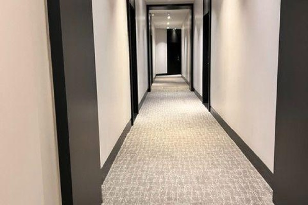 Long building hallway with carpeted floor and white walls with dark trim. - 293 The Kingsway, Toronto