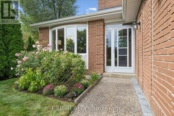 Front entrance with a glass door, walkway, bay window with flowers, and brick exterior. - 2932 Inlake Court, Mississauga