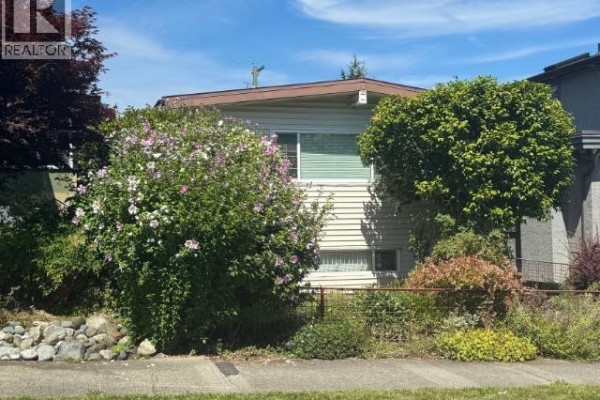Front exterior of the house at 2935 Adanac Street, with beige siding and abundant greenery. - 2935 Adanac Street, Vancouver