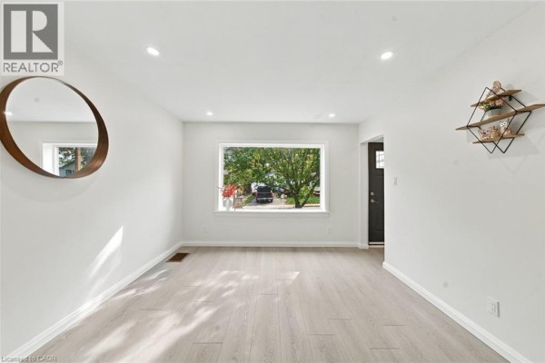 Empty living room with white walls, light wood laminate floors, and a decorative mirror. - 294 East 28th Street, Hamilton
