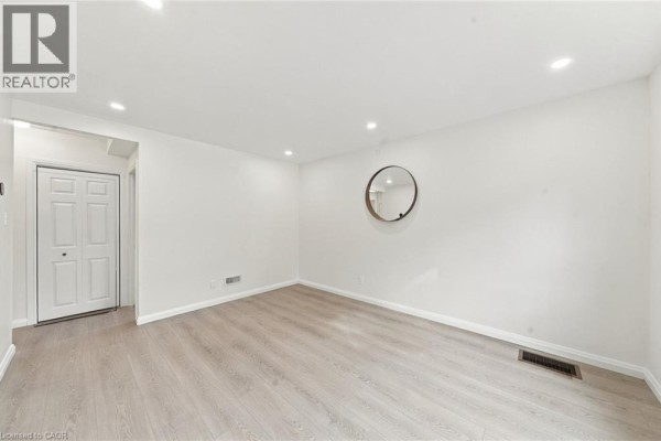 Spacious living room with white walls, light wood laminate flooring, and closet doors. - 294 East 28th Street, Hamilton
