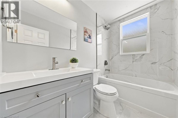 Bathroom with grey vanity, white countertop, toilet, bathtub, and marble tile shower surround. - 294 East 28th Street, Hamilton