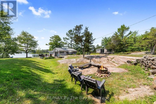 Exterior of the house showing a large wooden deck with outdoor furniture and a barbecue grill. - 294 Prisque Road, Georgian Bay
