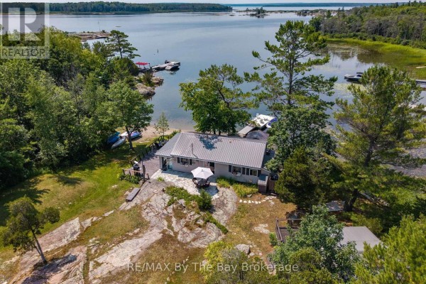 View of a wooden deck and water access with a dock and boats on the lake, framed by trees. - 294 Prisque Road, Georgian Bay