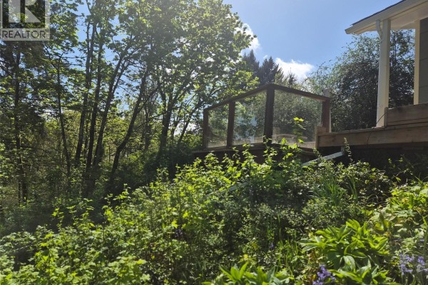 Wooden deck with glass railing surrounded by trees and lush green foliage. - 2942 Sherman Rd, Duncan