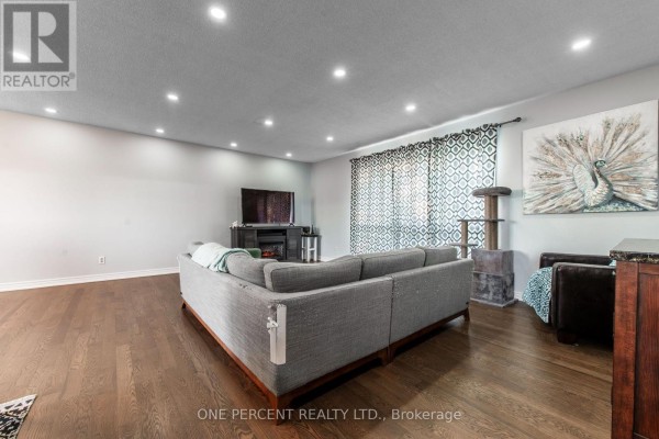 Living room with a grey sectional sofa, dark hardwood floors, recessed lighting, and a large window with patterned curtains. - 294235 8th Line, Amaranth