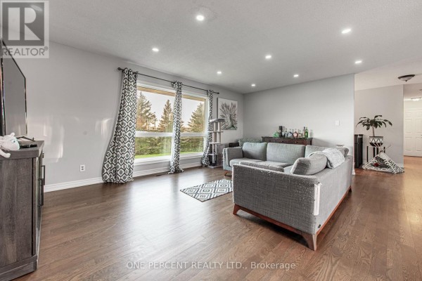 Living room with two large windows offering views of trees and fields, grey sofa, hardwood floors, and recessed lighting. - 294235 8th Line, Amaranth