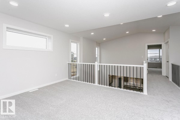 Spacious upstairs landing with grey carpet and black metal railing overlooking below. - 2944 65 St Sw, Edmonton