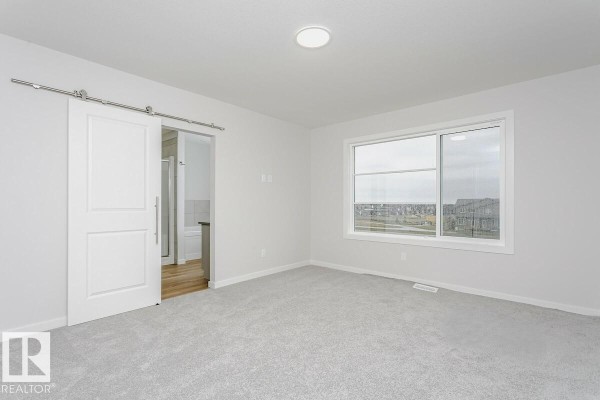 Bedroom with grey carpet, large window, and a white sliding barn door. - 2944 65 St Sw, Edmonton