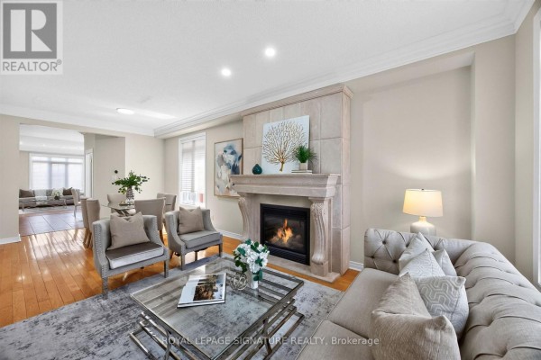 Living room with a stone fireplace, tufted sofa, and armchair facing a glass coffee table. - 2948 Bur Oak Avenue, Markham