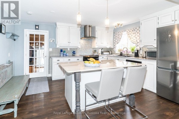 White kitchen featuring a stainless steel refrigerator, island, and glass-paned door. - 295 Bishop Street, Gravenhurst)
