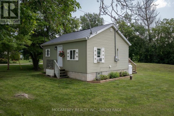 Side view of a small, light green house with a metal roof and propane tank. - 2956 County Road 14, Stone Mills