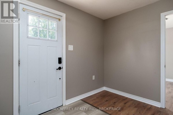 Interior view of the entrance foyer with a white door, grey walls, and wood-look floor. - 2956 County Road 14, Stone Mills