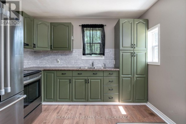 Kitchen with sage green cabinets, white brick backsplash, stainless steel appliances, and wood floor. - 2956 County Road 14, Stone Mills