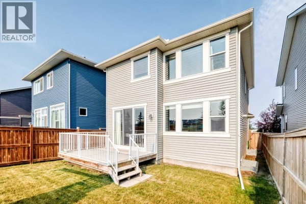View of a backyard from the side, featuring a wooden deck and stairs leading to a two-story house with grey siding. - 296 Nolancrest Heights Nw, Calgary