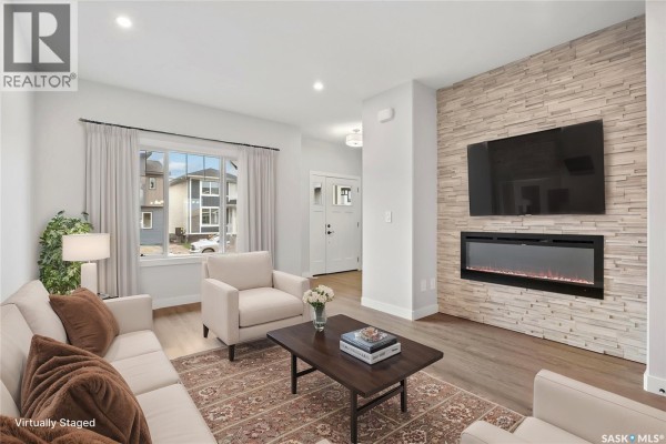 Living room with a grey sofa, two chairs, dark coffee table, and stone feature wall with TV. - 2960 Green Turtle Road, Regina