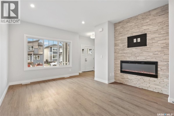 Living room with light wood flooring, white walls, and a large window overlooking the street. - 2960 Green Turtle Road, Regina