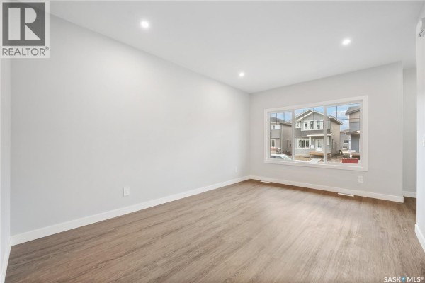 Empty room with light wood floors, white walls, and a large window with a view of houses. - 2960 Green Turtle Road, Regina