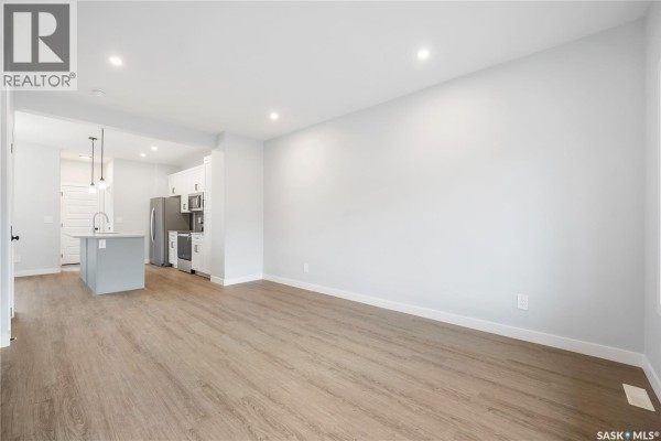 Open concept living area with light wood floors, white walls, showing a kitchen with island and appliances. - 2960 Green Turtle Road, Regina