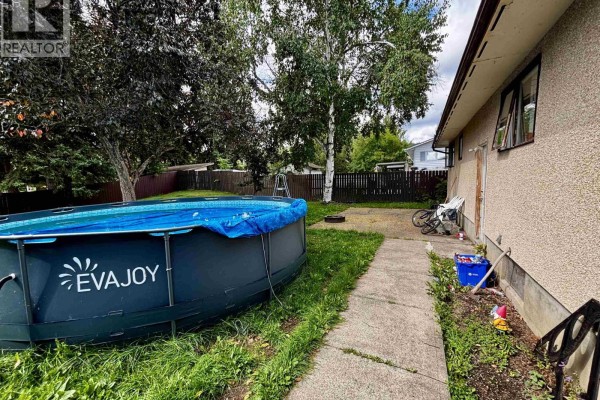 A backyard with a large above-ground pool, a concrete walkway, and a chain-link fence. - 2963 Pinewood Avenue, Prince George