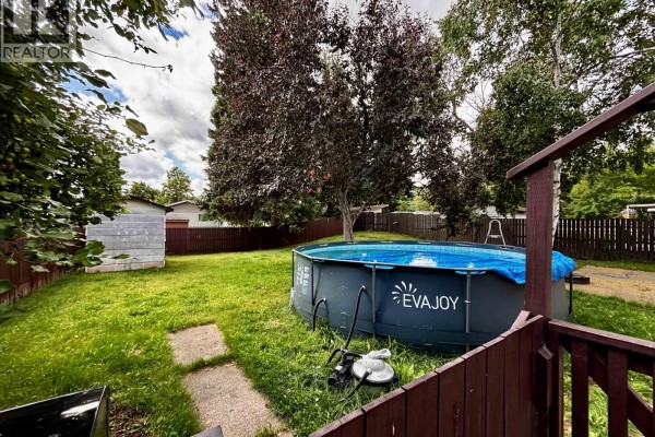 A backyard with a circular above-ground pool, a wooden deck railing, and mature trees. - 2963 Pinewood Avenue, Prince George