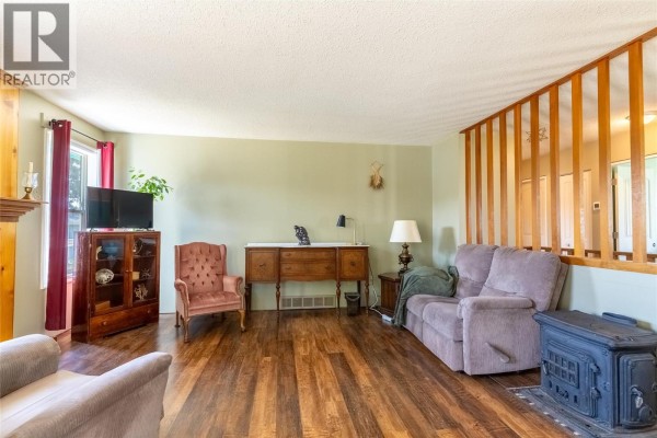 Living room featuring a wood-burning stove, wood floors, light green walls, and paneled divider. - 297 Chestnut Court, Logan Lake