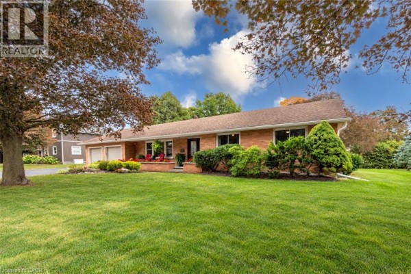 Wide angle exterior view of the brick house with manicured lawn and mature trees under a cloudy sky. - 297 Main Street W, Otterville