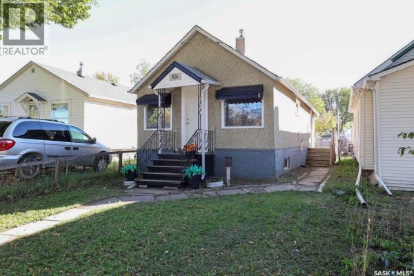 Front exterior view of a light-colored stucco house with a pitched roof and a small porch. - 297 Smith Street, Regina