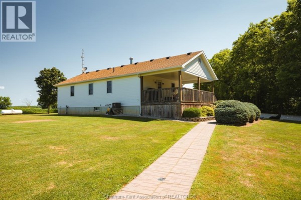 Brick pathway leading to the side of a white bungalow with a covered porch and lawn. - 29712 Esterville Road, Dresden