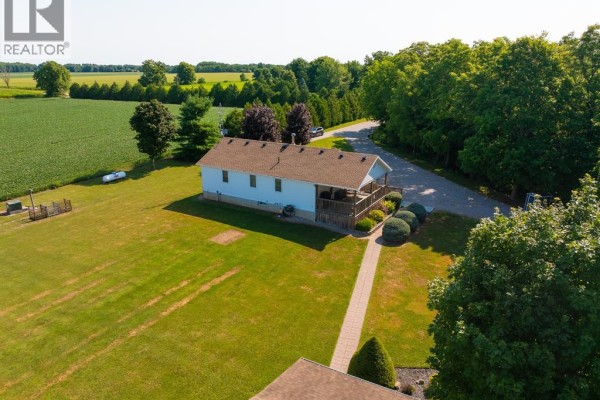 Aerial view of a white bungalow with a large wooden deck and surrounding green fields and trees. - 29712 Esterville Road, Dresden
