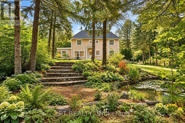 Stone steps lead down a lush, wooded garden with a small pond and lily pads, towards the rear of a light yellow stucco house. - 298 Wees Road, Uxbridge