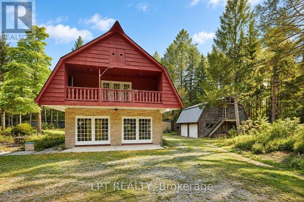 A red barn-style building with a stone base and large windows sits on a grassy lawn next to a smaller wooden outbuilding. - 298 Wees Road, Uxbridge