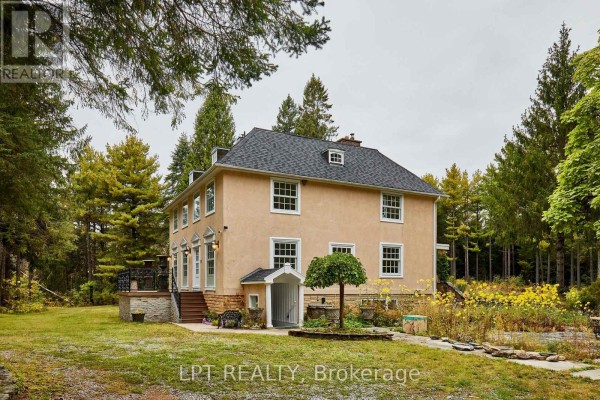Side view of a light yellow stucco house surrounded by mature trees, featuring a small covered entrance and a formal garden area. - 298 Wees Road, Uxbridge