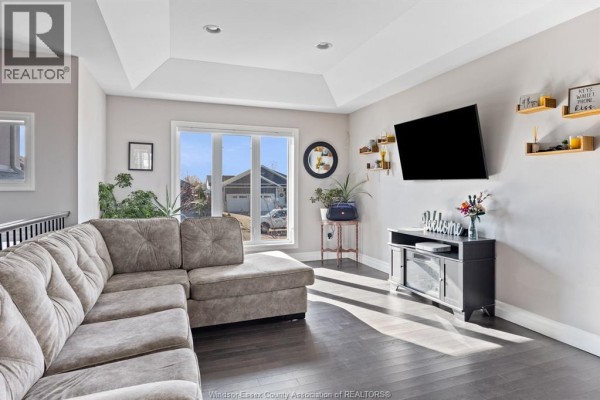 Living room with a large sectional sofa, a wall-mounted TV, and a bay window with natural light. - 298 Welsh Avenue, Amherstburg